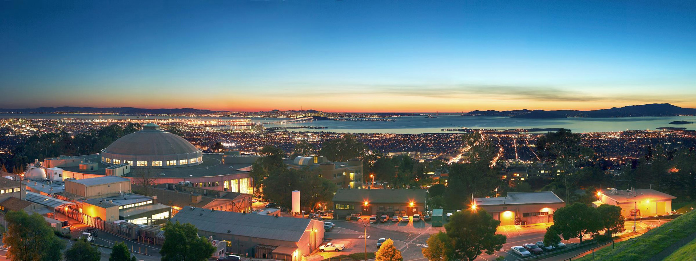 Sunset view of the lab and the San Francisco Bay with illuminated buildings.