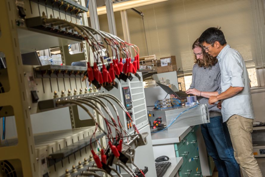 Two men in a laboratory test electronic equipment with a laptop.