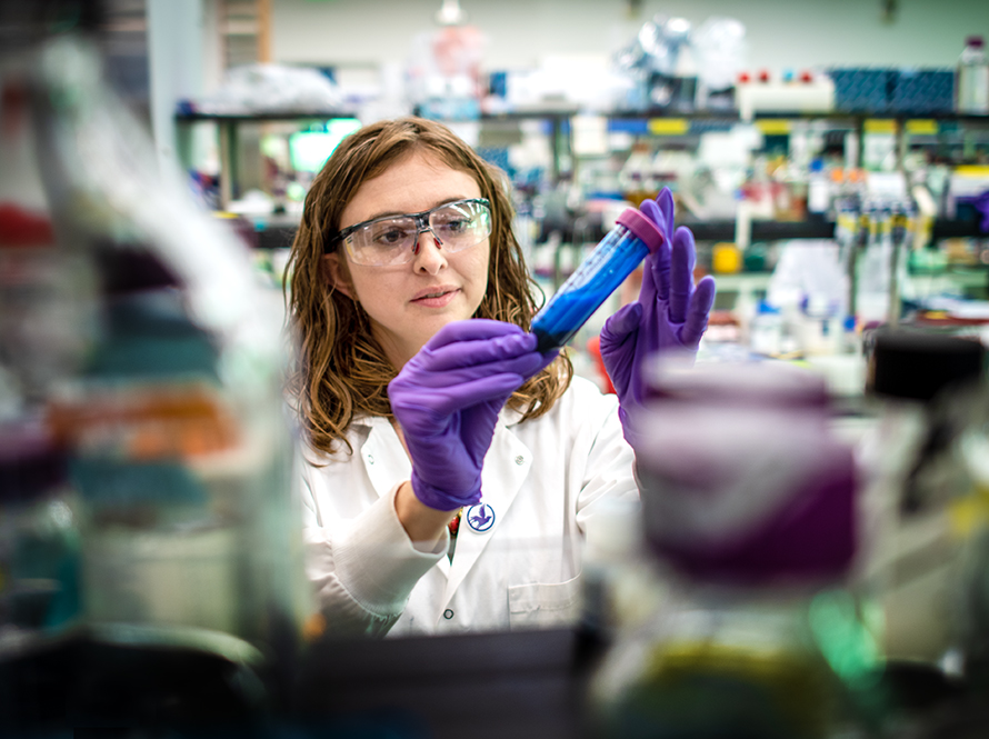 A young woman in a lab coat works in a laboratory with vials.