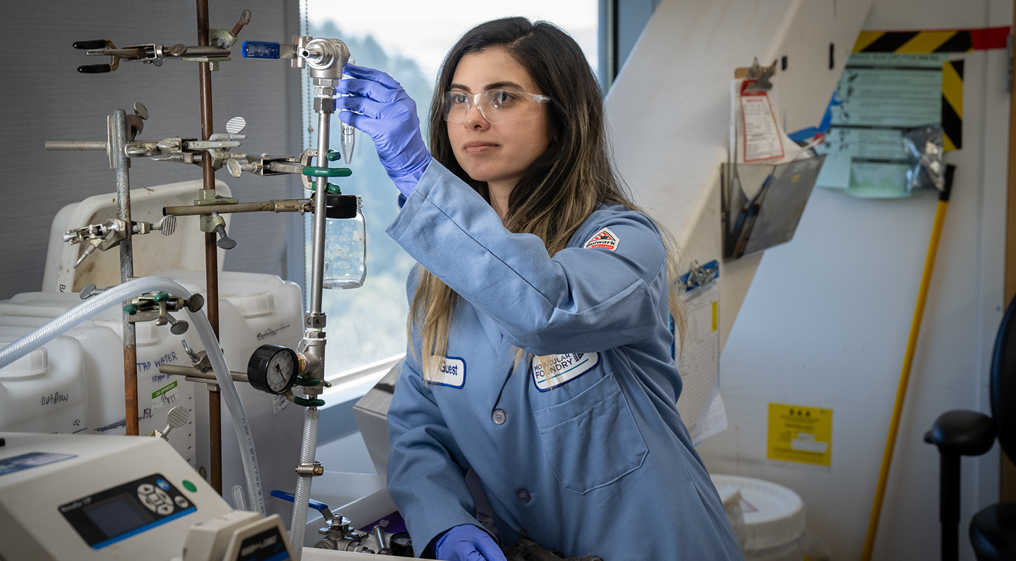 A research in blue protective safety equipment adjusts various pipes in the Molecular Foundry.
