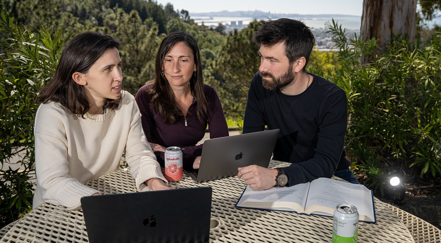 Three people work on laptops on an outdoor patio overlooking the San Francisco bay.