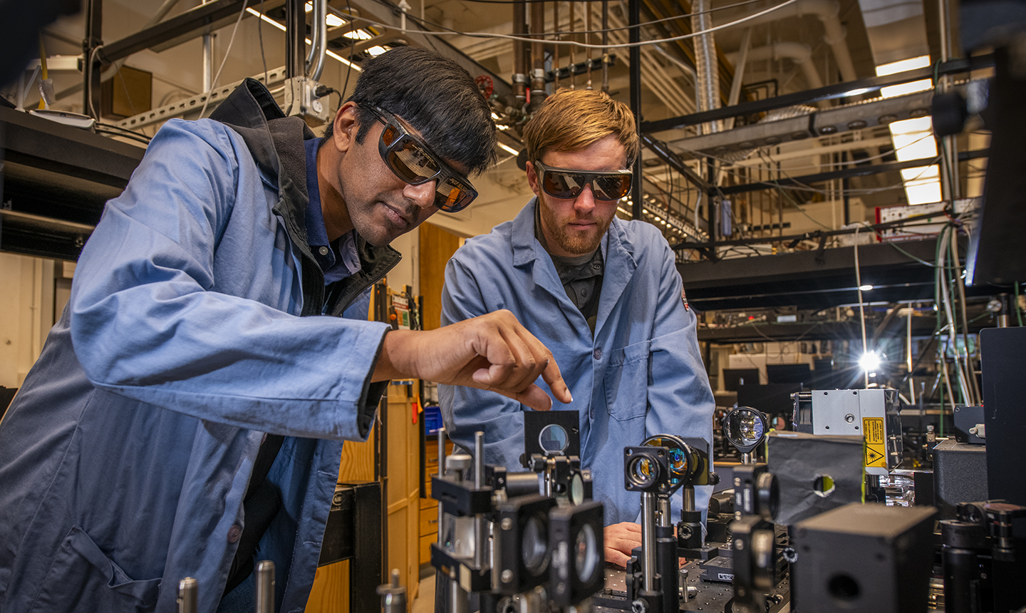 two scientists in blue coats looking at magnifying equipment